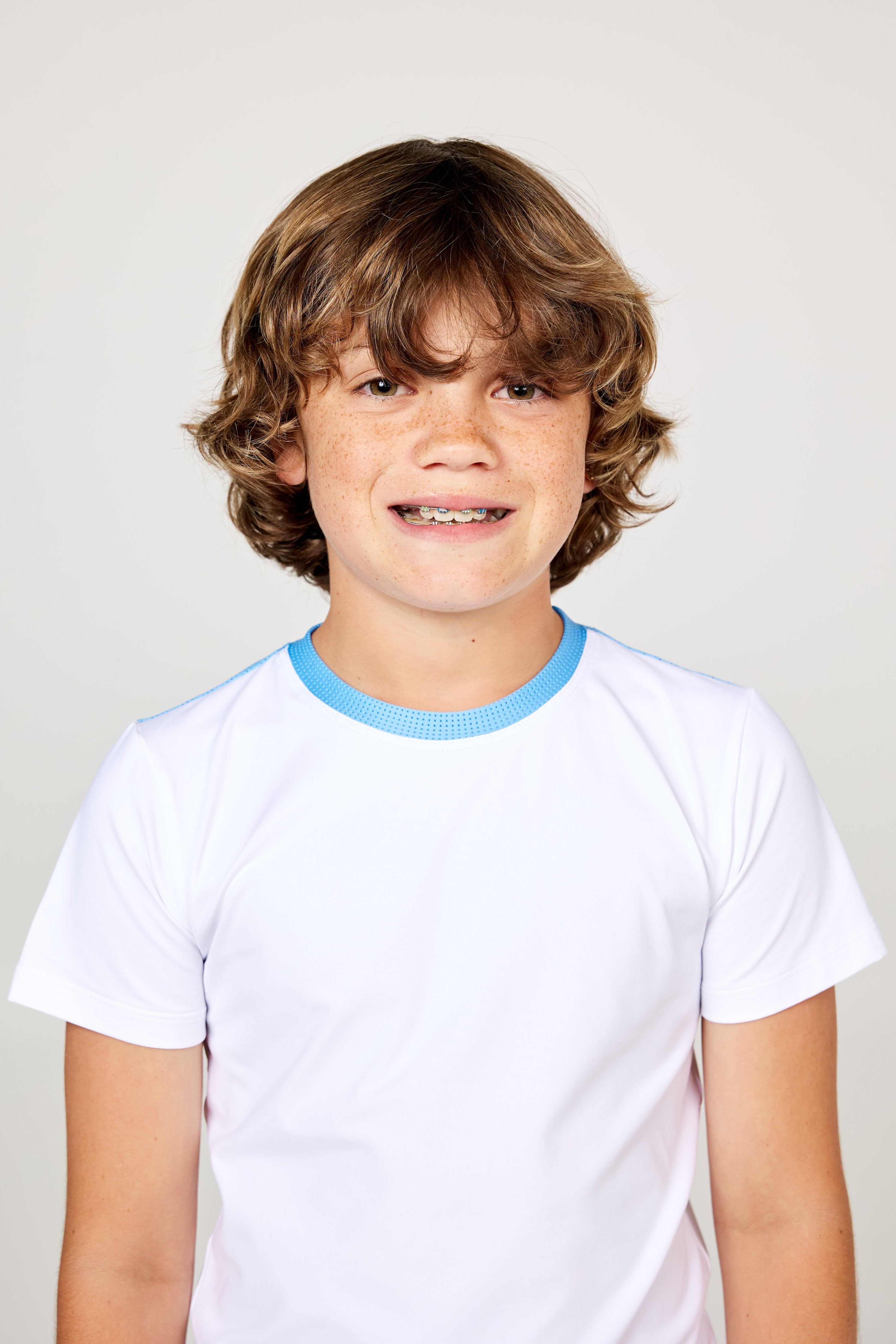 White boys' short sleeve tennis top by Sofibella, front detail view on model